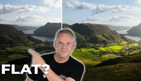 Man in black shirt pointing at mountainous valley landscape with bay and green fields.