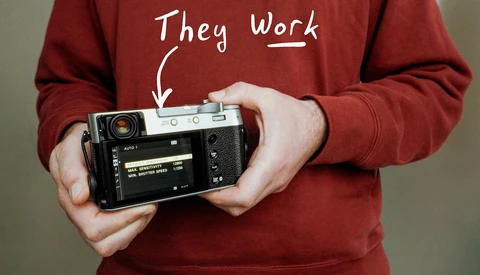 Person in burgundy sweatshirt holding a vintage rangefinder camera with annotation pointing to it saying 'They Work.'