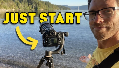 Photographer with camera mounted on gimbal stabilizer by a lakeside, demonstrating video equipment setup.