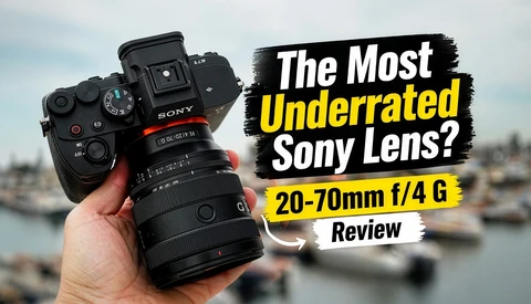 Sony camera with 20-70mm f/4 G lens held in hand against blurred waterfront background.
