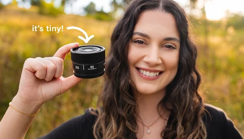 Photographer holding a compact camera lens outdoors with a blurred field background.