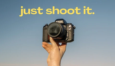 Hand holding a Nikon DSLR camera against a clear blue sky.