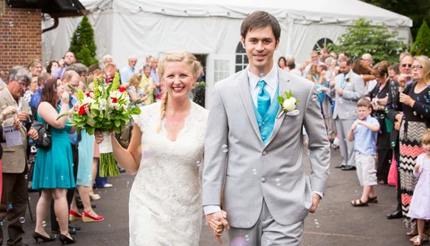 Bride and groom walking hand in hand through outdoor tent reception with guests lining both sides