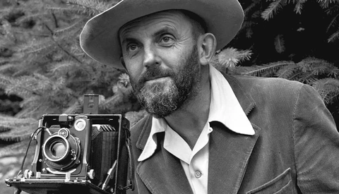 Bearded man in cowboy hat posing with a large format camera outdoors