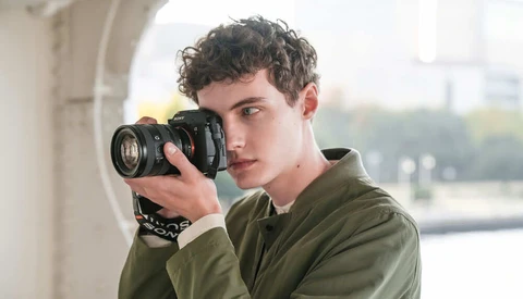 Young photographer holding DSLR camera with telephoto lens to eye while looking toward camera