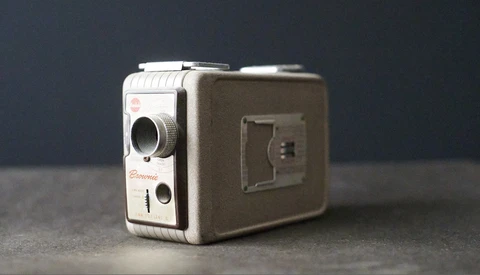 Vintage 8mm film camera with cream and brown two-tone body displayed against dark gray background