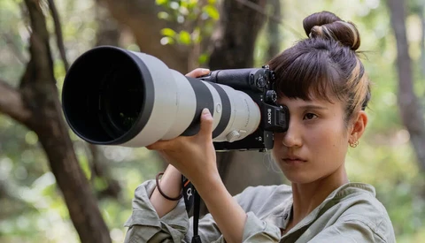 Young woman holding a telephoto lens to her eye in a wooded outdoor setting