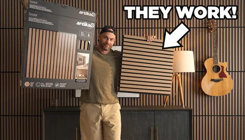 Man demonstrating acoustic panels mounted on wooden slat wall with arrow pointing to installed panels