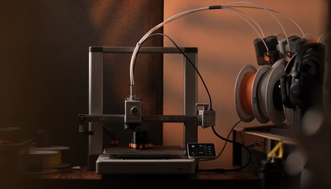 3D printer with filament spool and monitoring headphones on warm-toned studio backdrop