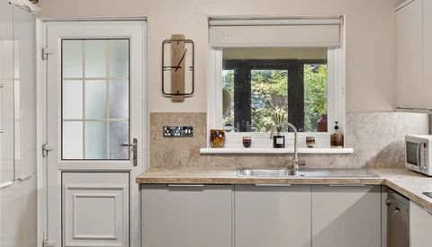 Modern kitchen with gray cabinetry, stone countertops, and garden views through large windows
