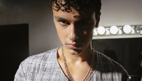 Portrait of young man with curly dark hair wearing gray shirt and chain necklace