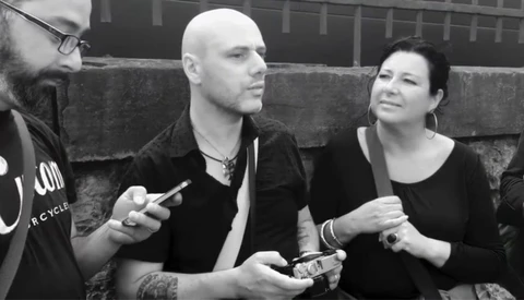Three people sitting on concrete steps in black and white, engaged in conversation while holding mobile devices