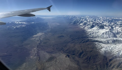 Aerial view from airplane window showing snow-capped mountain range and valleys below