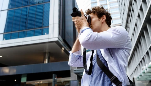 Photographer in light blue shirt holding camera up to compose shot in urban downtown setting