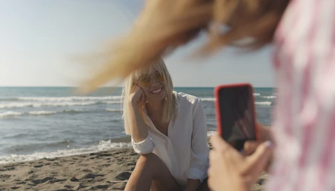 Woman posing for a smartphone photo on a beach at golden hour
