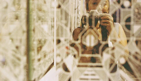 Photographer with camera reflected in mirror surrounded by reflective surfaces