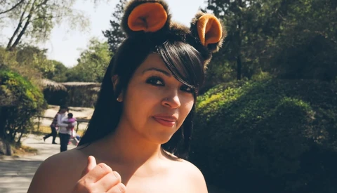 Woman with orange bear ear headband smiling at camera in sunlit outdoor garden setting