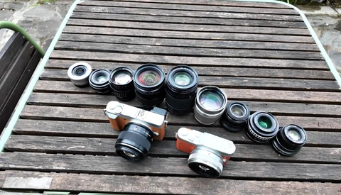 Collection of vintage rangefinder camera lenses and two film camera bodies arranged on wooden surface