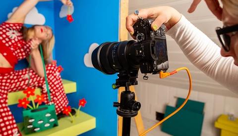 Photographer adjusting mirrorless camera on tripod during product photography shoot with colorful backdrop