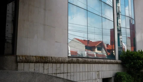 Reflective glass facade mirrors residential buildings with red roofs against concrete brutalist architecture