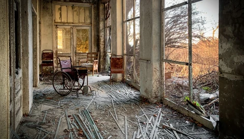 Abandoned institutional corridor with wheelchair and scattered debris, warm window light
