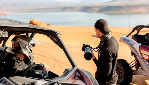 Photographer with telephoto lens shooting beside off-road vehicles overlooking desert reservoir landscape