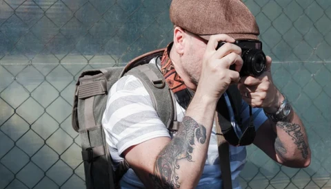 Photographer with camera and backpack shooting against chain-link fence