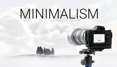 Mirrorless camera on tripod with telephoto lens pointed at minimalist landscape with three trees