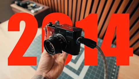 Hand holding a vintage black film camera with red typography overlay reading "2014"
