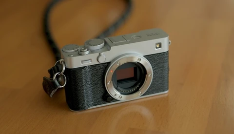 Rangefinder camera with chrome top plate and black leather body, displayed on wooden surface with shoulder strap
