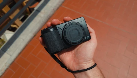 Ricoh GR compact camera held in hand against brick background