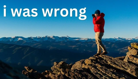 Person in red jacket standing on mountain peak overlooking alpine landscape
