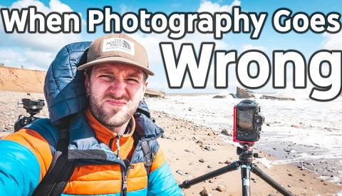 Photographer in blue and orange jacket holding camera on tripod at beach during golden hour