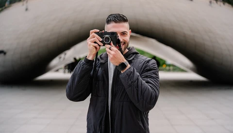 Photographer holding rangefinder camera to face while standing in front of curved concrete architectural structure