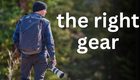 Photographer wearing backpack and beanie while holding telephoto lens in forest setting