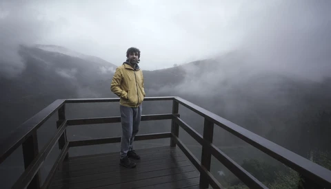 Person in yellow jacket standing on wooden observation deck overlooking misty forested mountains