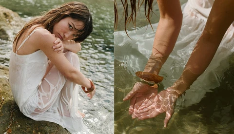 Woman in wet white dress sitting by water with hands in shallow stream