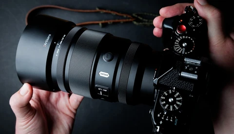 Photographer's hands holding mirrorless camera with telephoto lens against dark background