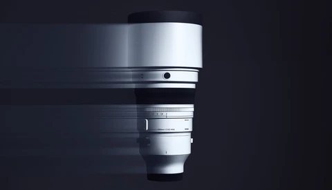 Silver telephoto lens with focus ring and distance scale against dark background