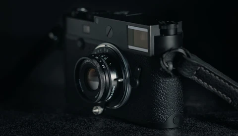 Black rangefinder camera with attached lens and shoulder strap on dark textured surface