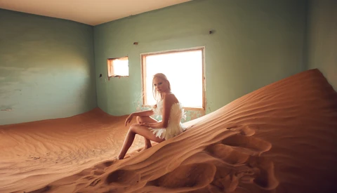 Woman posing on large sand dune inside minimalist room with green walls and bright doorway