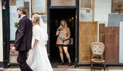 Bride and groom walking past storefronts with woman in doorway during street photography session