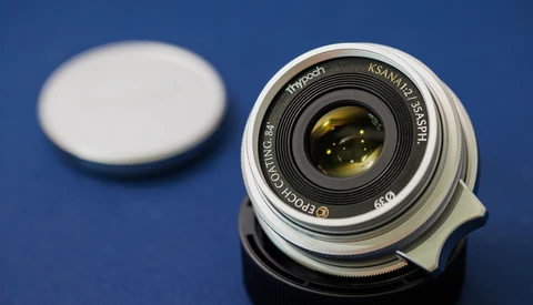 Vintage wide-angle lens with yellow-amber glass elements on blue background