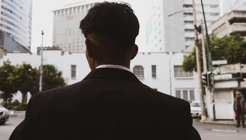 Man in dark suit viewed from behind facing urban downtown skyline