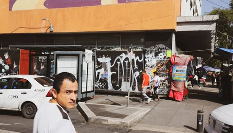 Man in white shirt posing on urban street with graffitied storefront and parked vehicles