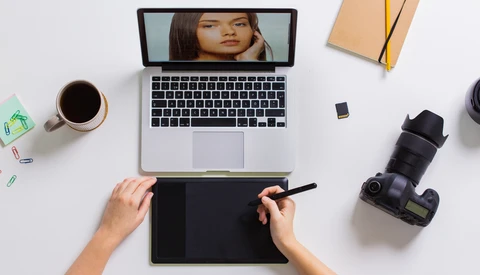 Photographer's overhead desk setup with laptop, graphics tablet, camera, and coffee