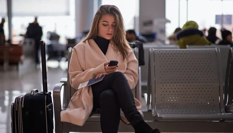 Woman in beige cardigan seated in modern airport terminal holding smartphone