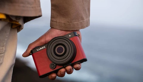 Person holding red Lumix compact camera with ocean backdrop