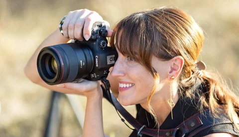 Female photographer holding a DSLR camera with telephoto lens, smiling while shooting outdoors