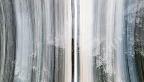 Aerial view of a snow-covered forest with a dark road cutting through the center